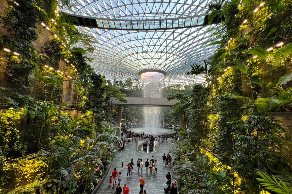 Visitors at Jewel traverse the ground floor, beneath the glass ceiling and Rain Vortex waterfall, in Singapore's Changi Airport.