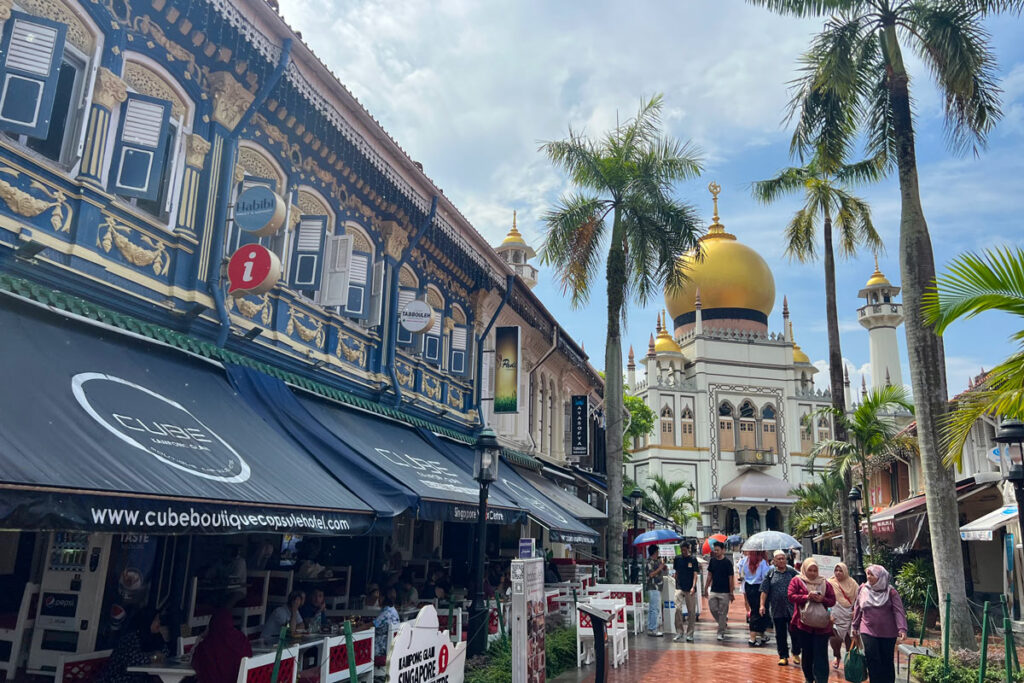 Pedestrians walk along Bussora Street in Singapore's Kampong Gelam neighborhood, with the large Sultan Mosque featured prominently in the background.