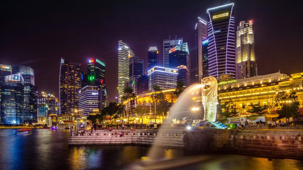 Singapore's famous Merlion Statue fountain spouts water into Marina Bay, with the downtown skyline illuminated at night in the background