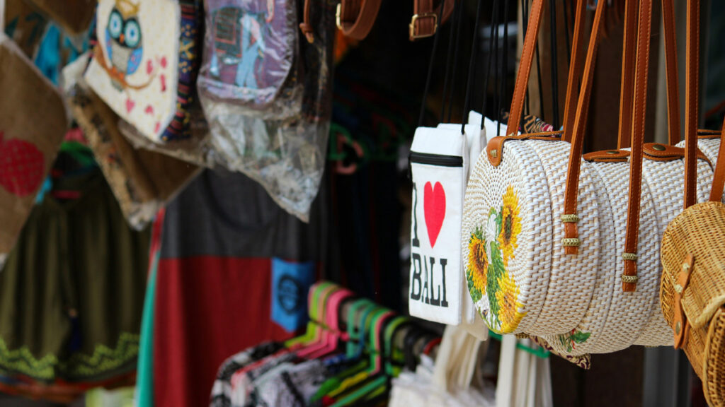 Souvenir purses and tote bags hang from a market stall in Ubud, Bali.