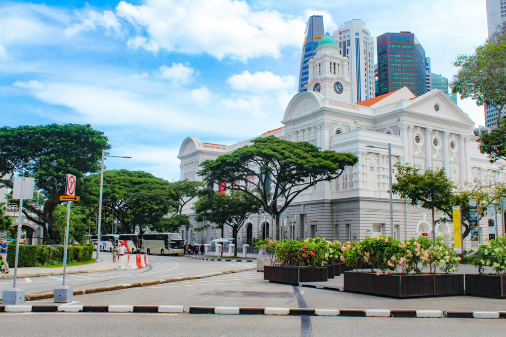 A building in Singapore's Colonial District, in a classical architecture style, stands in contract with modern skyscrapers behind it. 