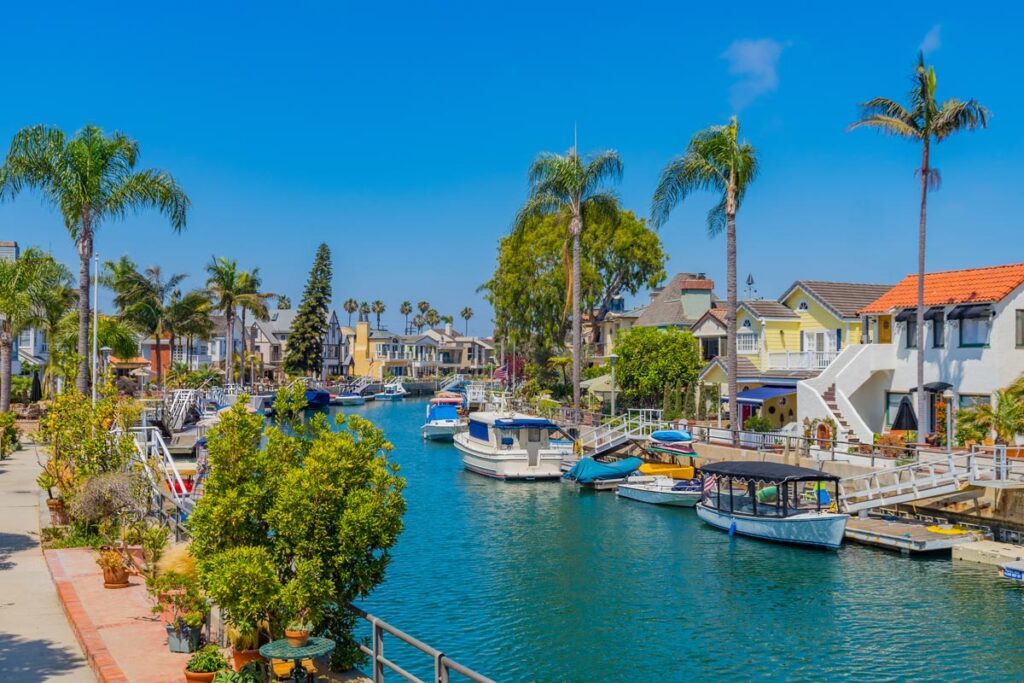 The Naples Canals in Long Beach, California offer protected waterways that are great to paddleboard in Los Angeles. The canals are shown here on a sunny day, with small leisure boats dotting the water and tall palm trees lining the footpaths.