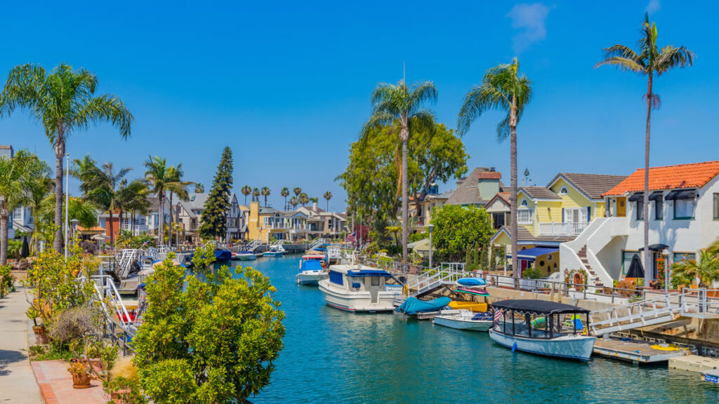 The Naples Canals in Long Beach, California offer protected waterways that are great to paddleboard in Los Angeles. The canals are shown here on a sunny day, with small leisure boats dotting the water and tall palm trees lining the footpaths.