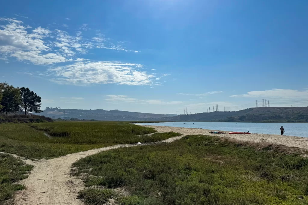 A sandy footpath winds through marshland to the shore of Agua Hedionda lagoon in Carlsbad, California. Agua Hedionda is one of the best places to paddle board in San Diego.