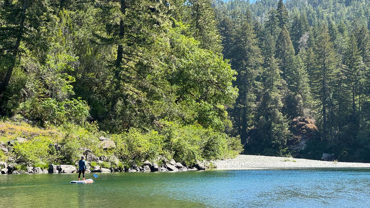 A female paddleboarder pauses along the Smith River, outside of Crescent City, California. This is one of the best places for paddle boarding and kayaking near Redwood National Park.