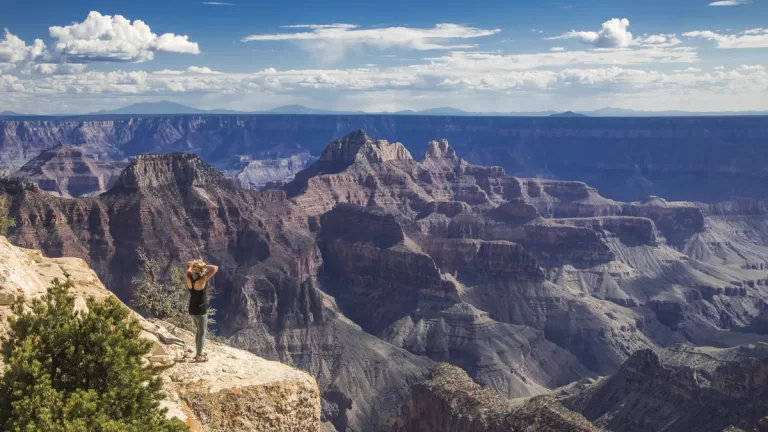 A female hiker pauses to catch her breath on a stone promontory, as she gazes out over the Grand Canyon stretching to the horizon.