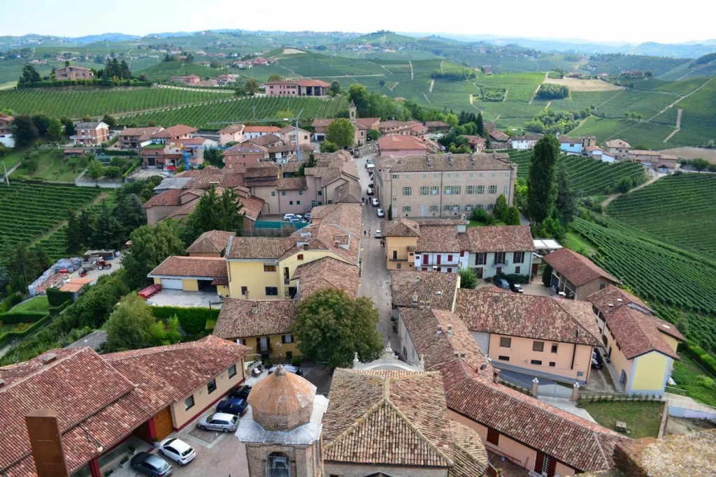 The view from the top of Torre Barbaresco in Piedmont, Italy, overlooks the terracotta roofs of the small town of Barbaresco, surrounded by green vineyards.