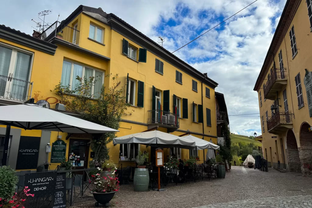 Bright yellow-painted buildings frame a cobblestoned pedestrian street and al fresco cafe in the small town of Barolo. When choosing where to stay in Piedmont Italy, Barolo is one of the more popular villages in the region.