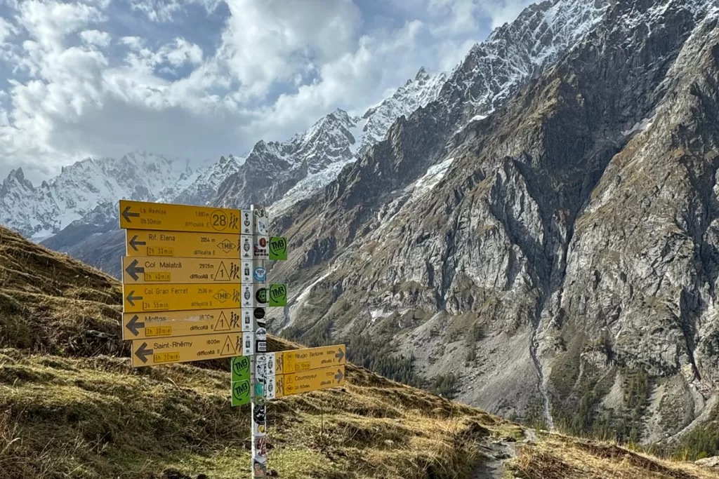 A signpost with numerous yellow trail markers denotes a footpath on a mountain ridge outside of Courmayeur, Italy.