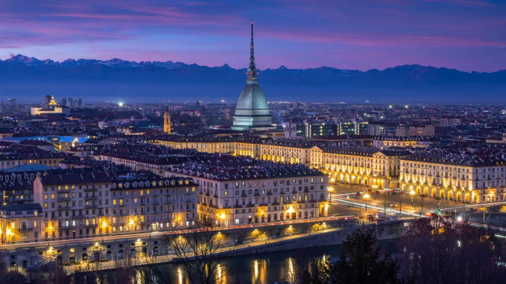 The iconic skyline of Turin, Italy is seen from Turin City View across the river, as dusk falls and the lights come on in the city.