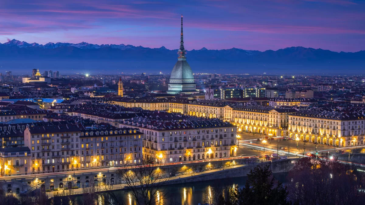 The iconic skyline of Turin, Italy is seen from Turin City View across the river, as dusk falls and the lights come on in the city.