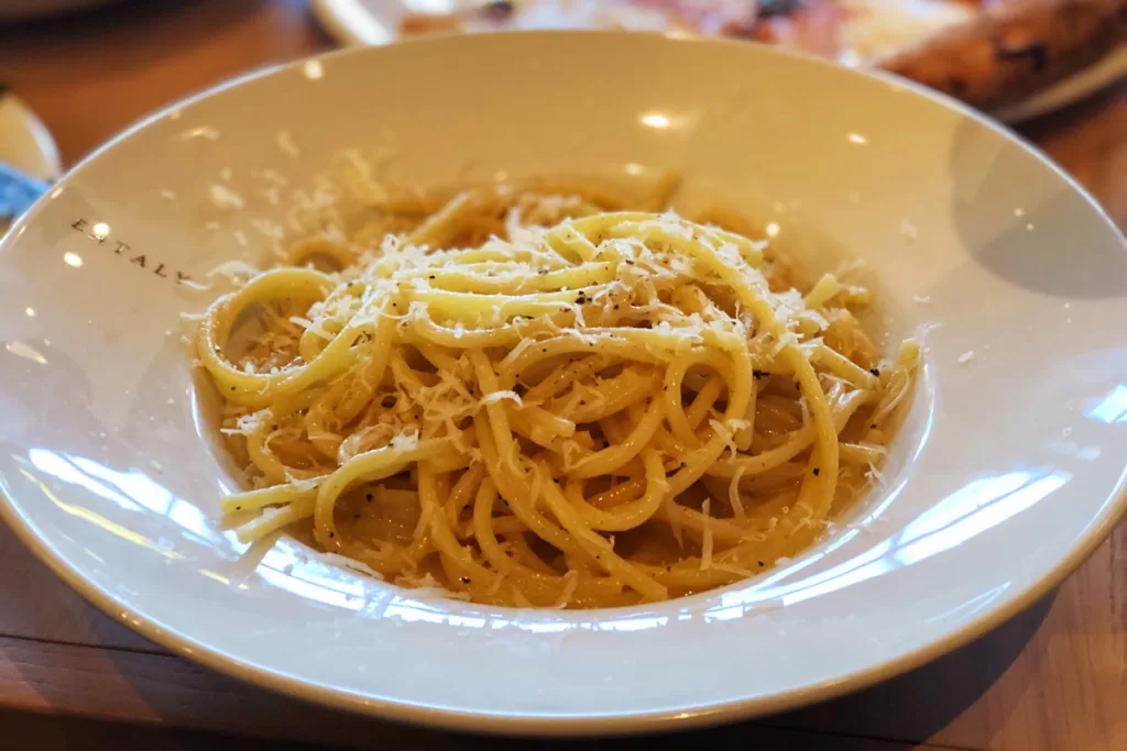 A bowl of cacio e pepe, one of the traditional Roman pastas, is served with bucatini noodles, pecorino cheese, and pepper. When choosing what to eat in Rome, cacio e pepe is one of the quintessential dishes.