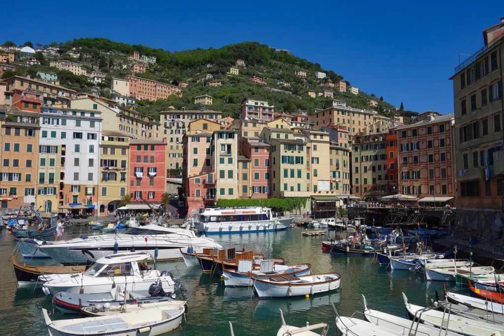 Small boats line the harbor in Camogli, Italy, surrounded by tall pastel-hued buildings rising up into the hillsides beyond.