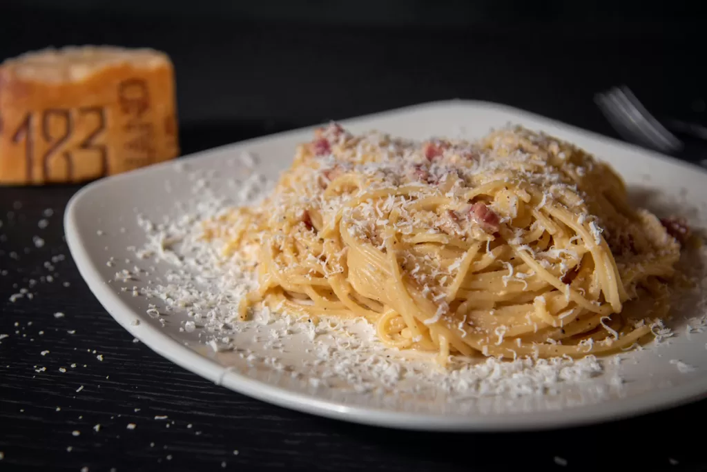 A plate of pasta alla Carbonara sits on a dark wood table. When choosing what to eat in Rome, carbonara is one of the quintessential dishes.