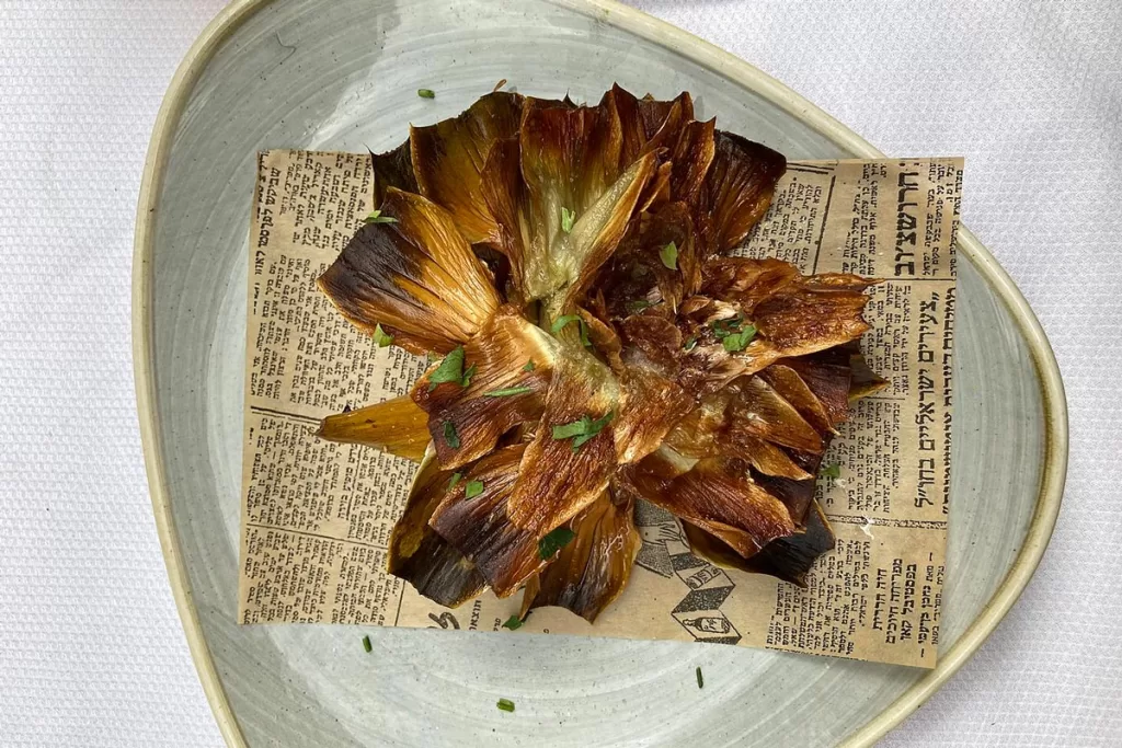 Carciofi alla Giudia, or Jewish-style artichokes, are artfully presented on a blue dish with newsprint. When deciding what to eat in Rome, artichokes are the iconic appetizer.