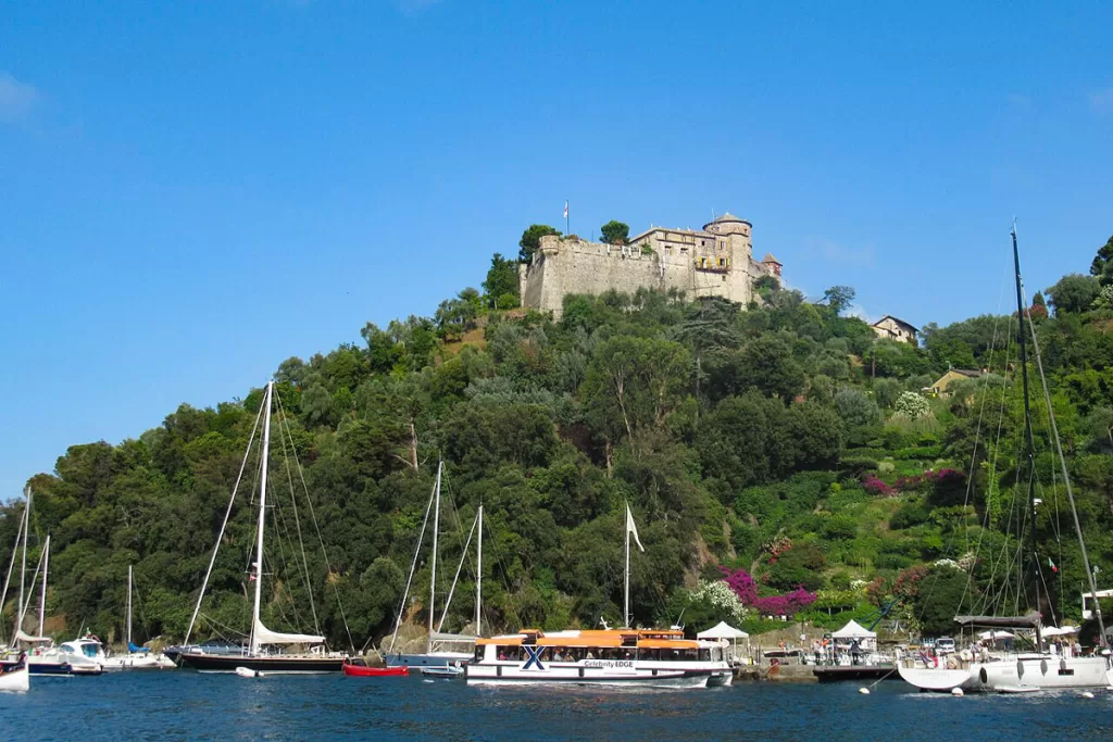 The iconic stone Castello Brown rises on a lush hillside above Portofino Harbor in Portofino, Italy. Visiting the castle is one of the most popular things to do in Portofino.