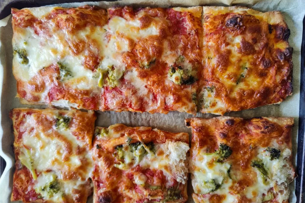 Six square pizza slices are cut in the Roman style, or pizza al taglio, and displayed on a tray.