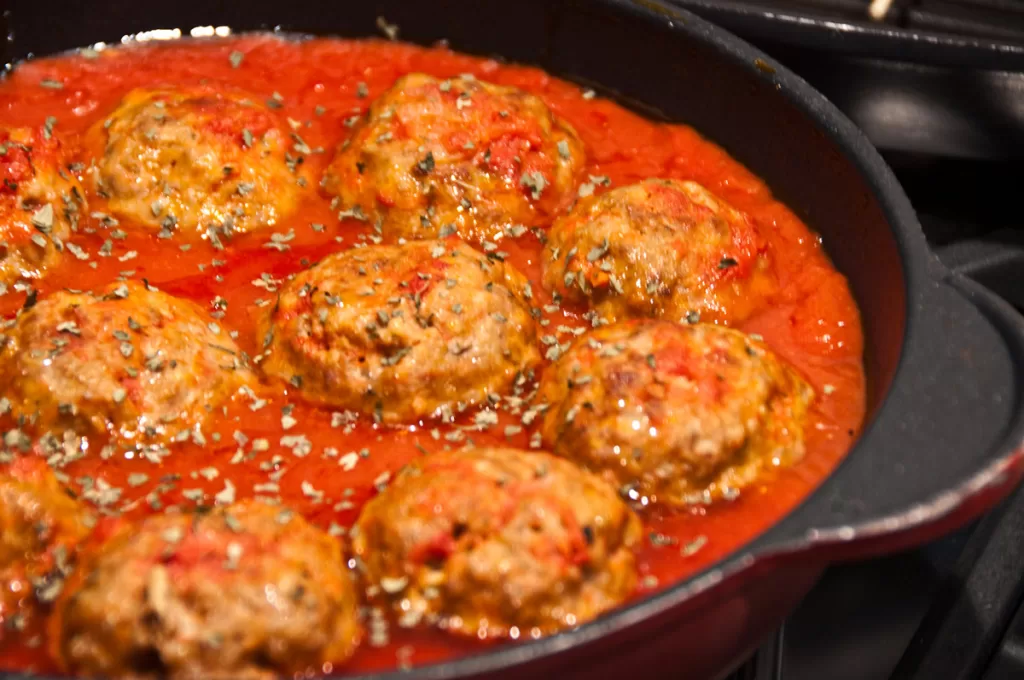 Polpette alla Romana, or Roman-style meatballs, simmer in a rich tomato sauce in an iron pan.