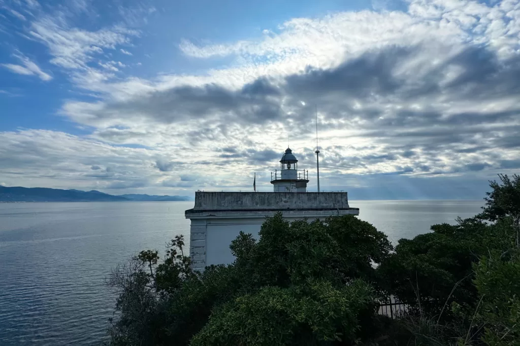 Faro di Portofino, or Portofino Lighthouse, looks out to distant hills across the Ligurian Sea on a partly cloudy day.