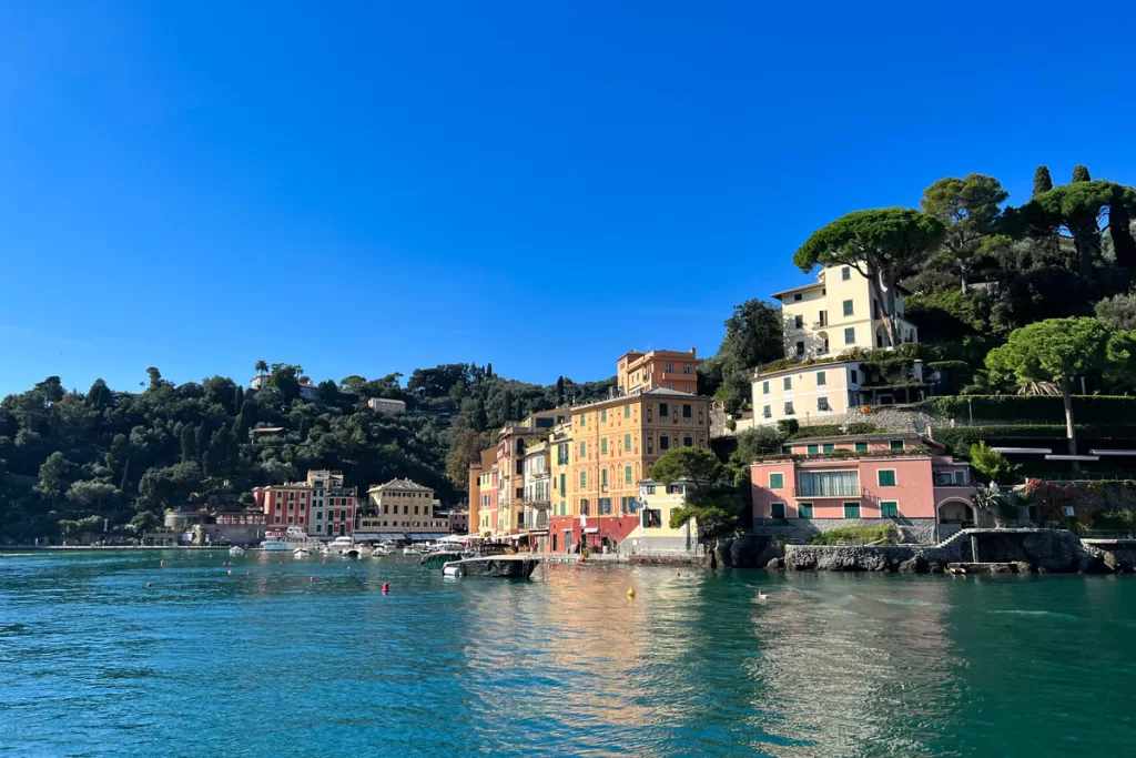 Pastel-hued homes line the water outside of Portofino, Italy on a sunny day.