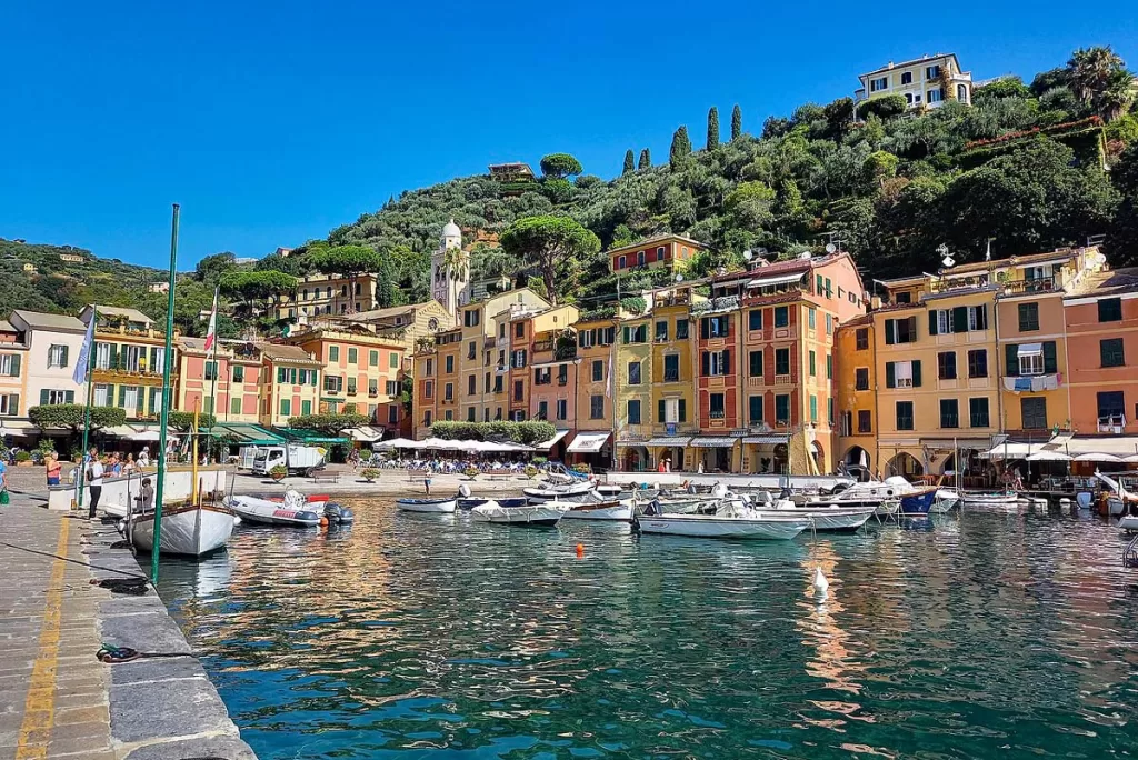 Colorful, pastel-hued homes line the waterfront of Portofino, Italy with small leisure boats drifting in the foreground. Walking the seaside promenade is one of the most popular things to do in Portofino.