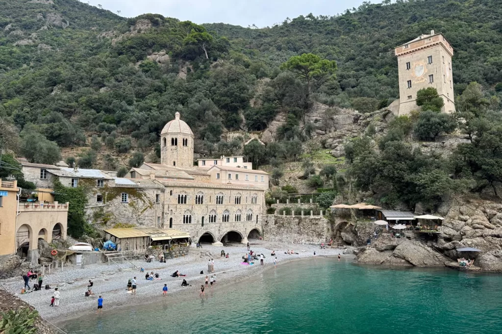 The honey-colored stone San Fruttuosto Abbey overlooks the aquamarine waters of its protected bay outside of Portofino, Italy. A day trip to the thousand-year-old abbey is one of the more popular things to do in Portofino.