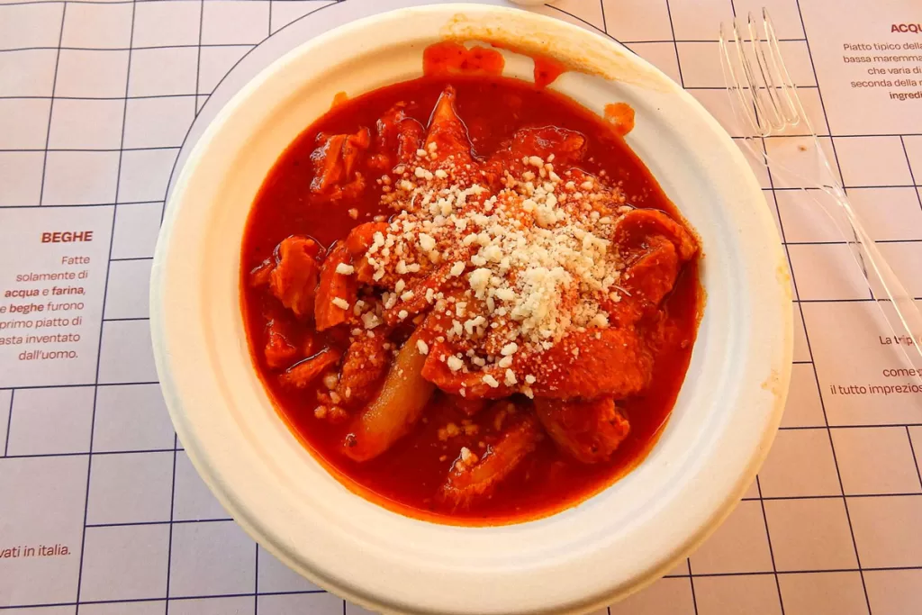 A bowl of Trippa alla Romana, or Roman-style tripe, is served in a rich tomato sauce and topped with pecorino cheese.