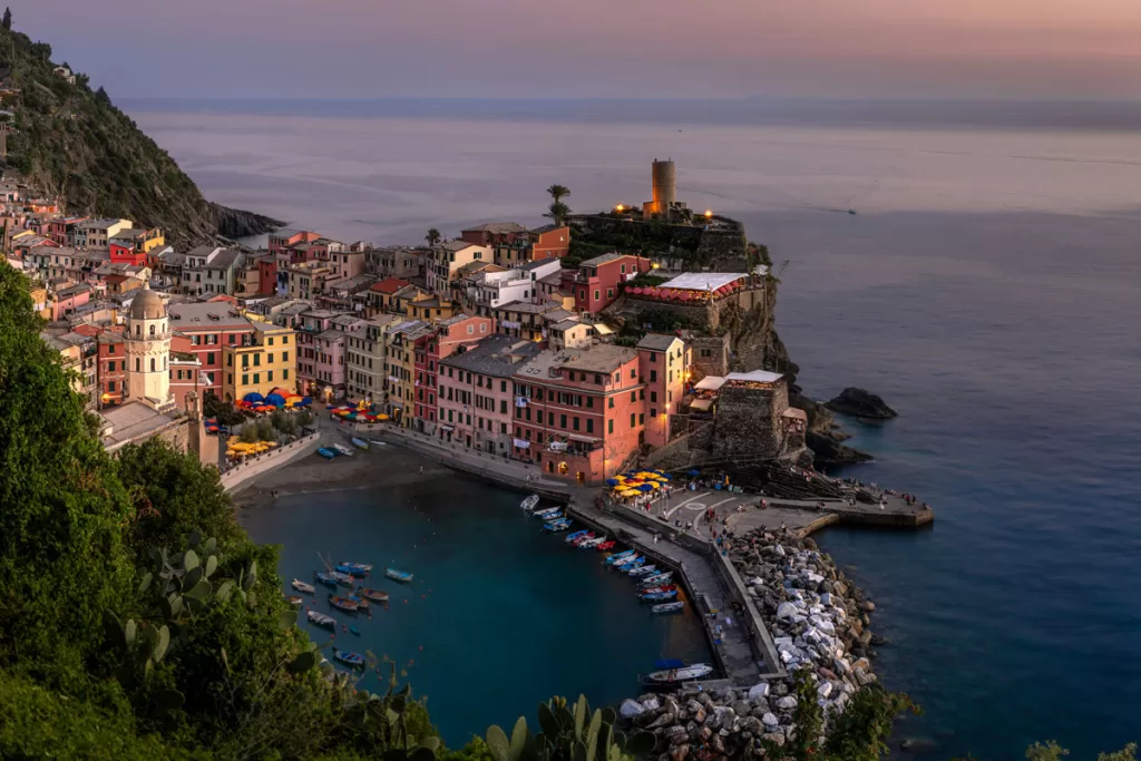 Sunset creates muted hues of Cinque Terre's famed photo spot, looking down on the town of Vernazza with its stone tower and boats dotting the harbor.