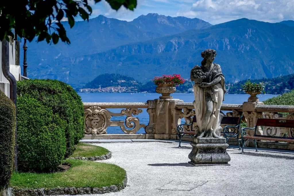 An antiquated stone statue of a woman stands against a backdrop of Lake Como and its surrounding hills in Italy's Lake District. When choosing where to go in northern Italy, the Lake District is one of the best spots for sheer relaxation.