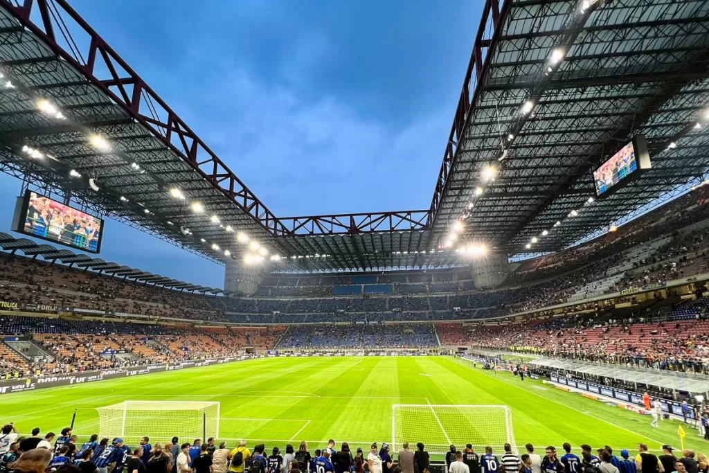 Lights turn on at dusk in Milan's iconic San Siro Stadium, as fans begin to arrive in anticipation of a football match.