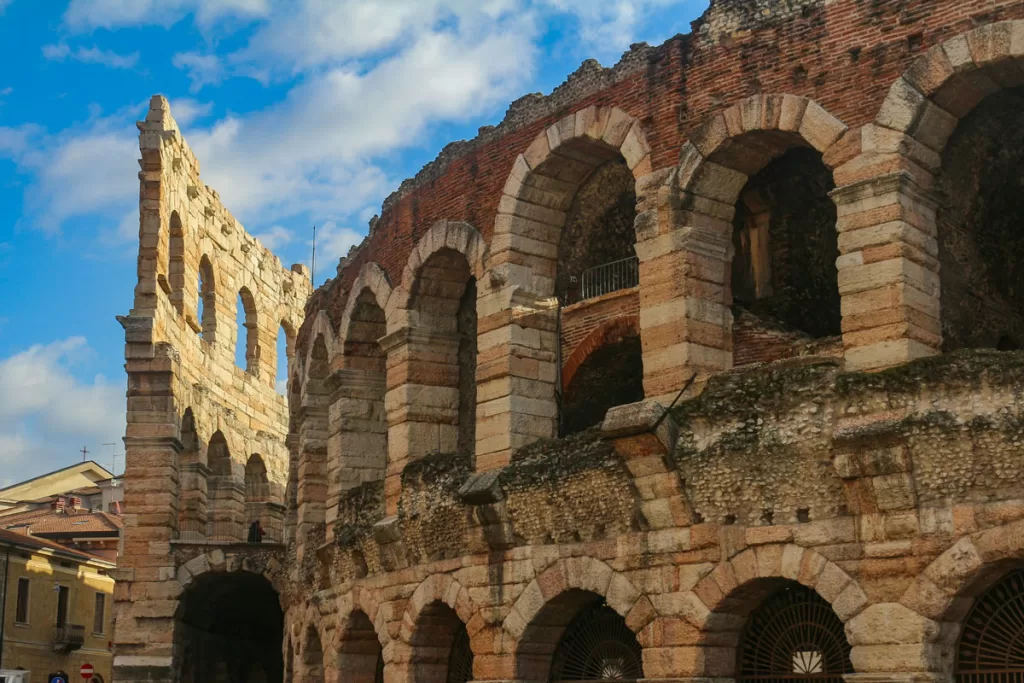 A closeup of the red brick and stone arches of the ancient Roman Arena in Verona, Italy, silhouetted against a bright blue sky.