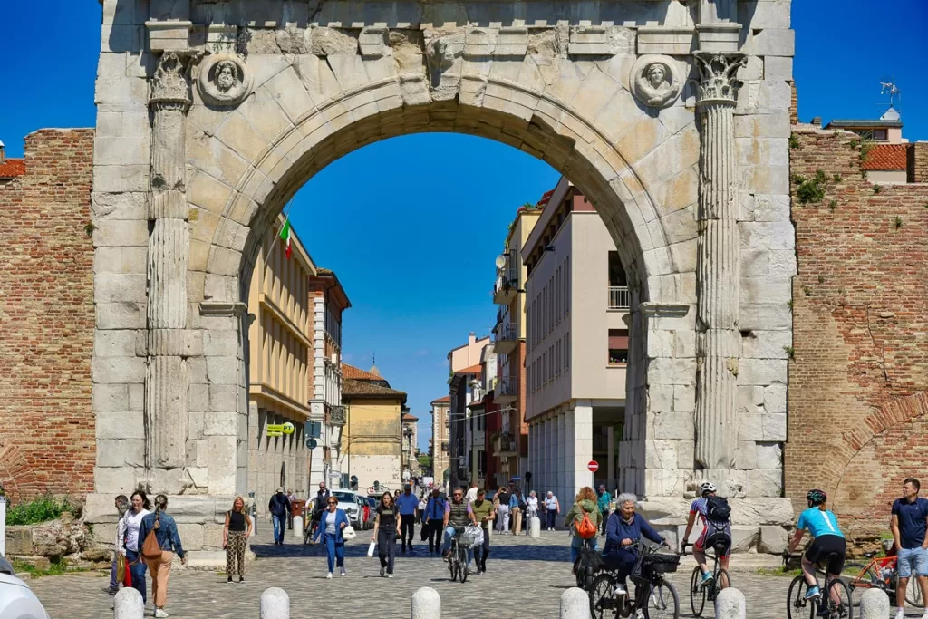 Pedestrians and bicyclists pass underneath the ancient Roman Arch of Augustus in Rimini, Italy.