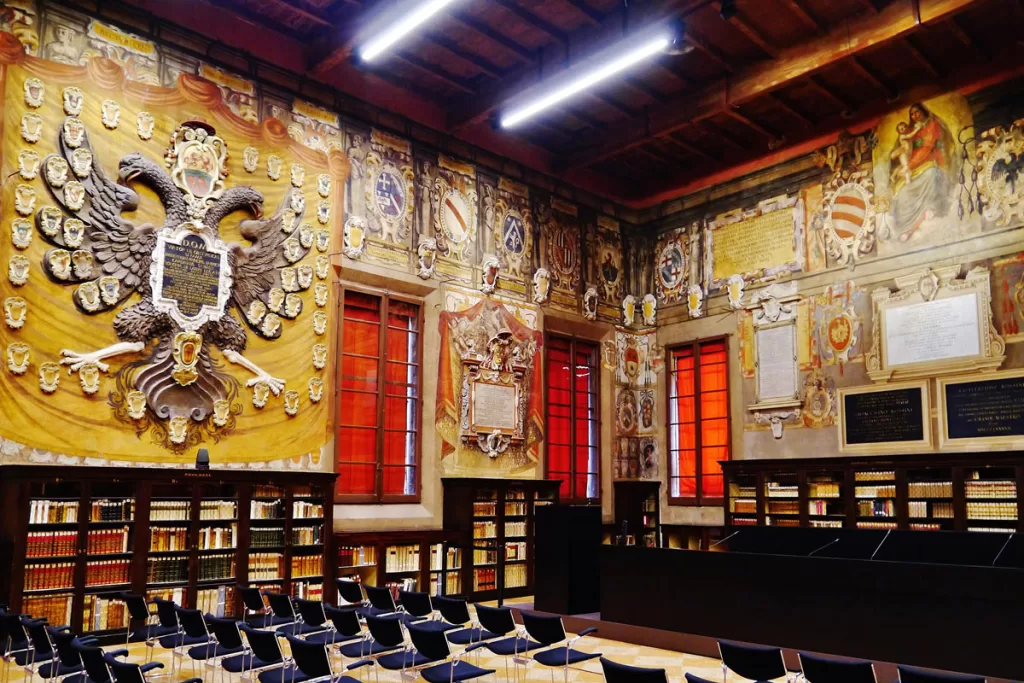 The interior of the storied Archiginnasio library at the University of Bologna, with walls covered with various seals and religious works.