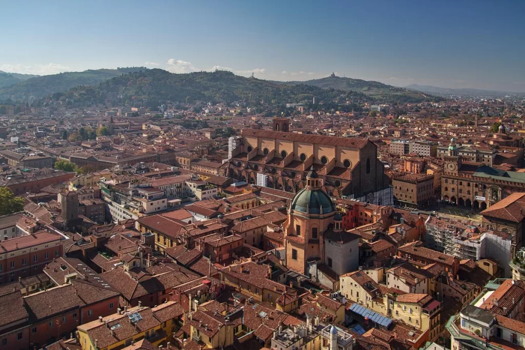 The view from the top of the Asinelli Tower in Bologna, Italy, looking over the surrounding terracotta rooftops and out to the distant hillsides.