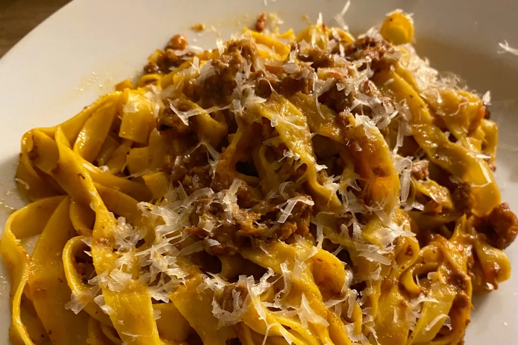 A close-up of a plate of tagliatelle bolognese with shaved Parmesan.