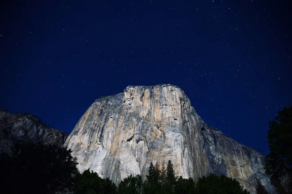 Stars twinkle over the illuminated face of El Capitan at night in Yosemite National Park.