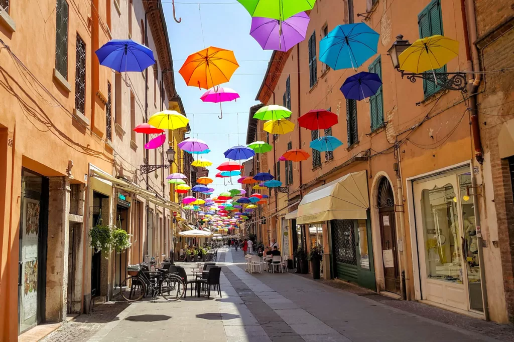 Colorful umbrellas hang above a narrow pedestrian street in Ferrara, Italy.
