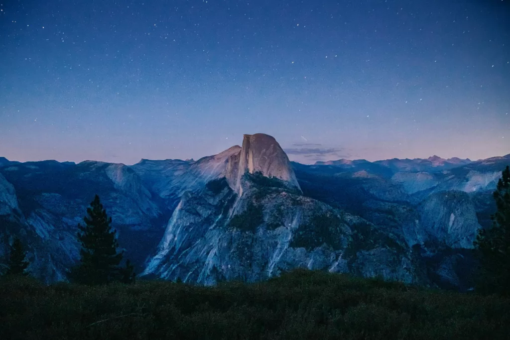 Twilight bathes Half Dome in purple light as stars twinkle overhead, in Yosemite National Park.