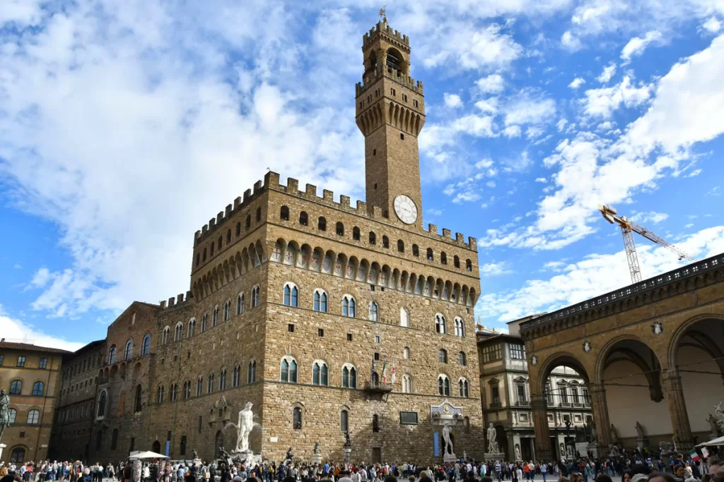 Crowds gather in Piazza della Signoria in Florence, Italy, beneath the towering facade of Palazzo Vecchio.
