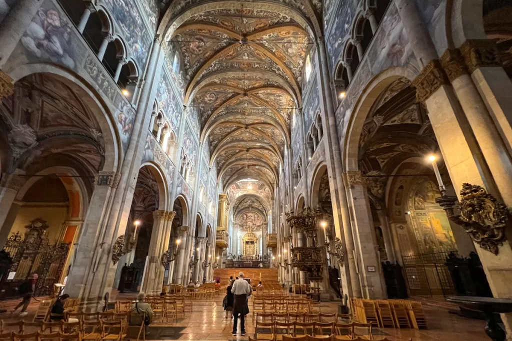 Patrons stand beneath the soaring frescoed arches and domed ceiling of the Duomo in Parma, Italy.