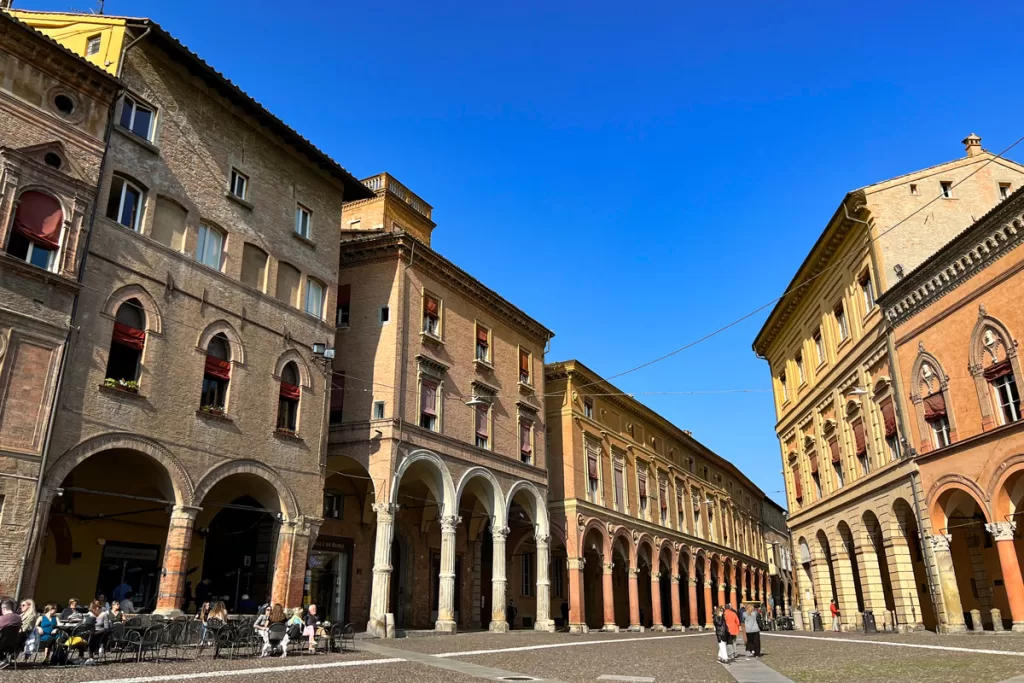 People sit at al fresco tables on the Piazza San Stefano in Bologna, Italy, surrounded by the city's iconic medieval porticos.