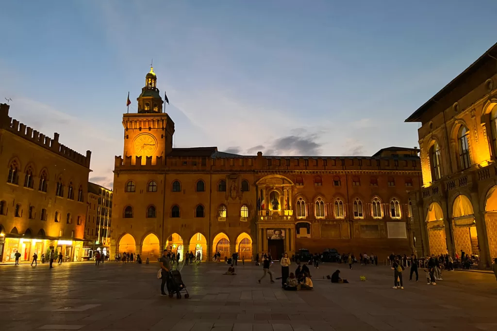 The medieval buildings flanking Piazza Maggiore in Bologna, Italy become illuminated as dusk falls over the square.