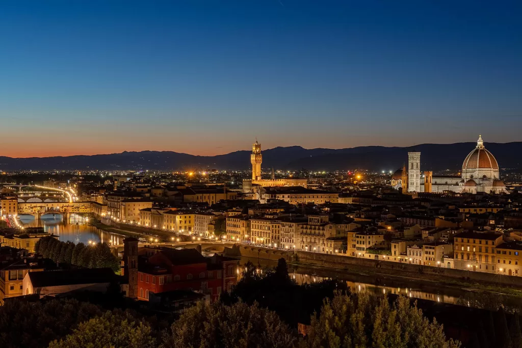 Twinkling lights come on at dusk in Florence, Italy, looking back to Santa Maria del Fiore and the Palazzo Vecchio from Piazzale Michelangelo.