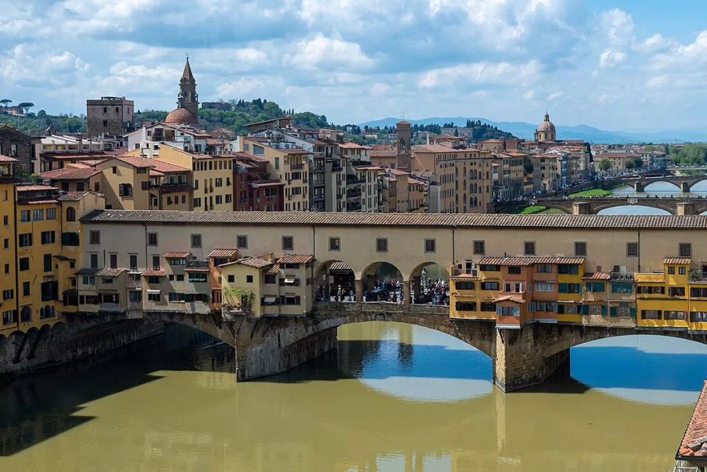 The medieval Ponte Vecchio spans the Arno River in Florence, Italy, surrounded by tall residential buildings.