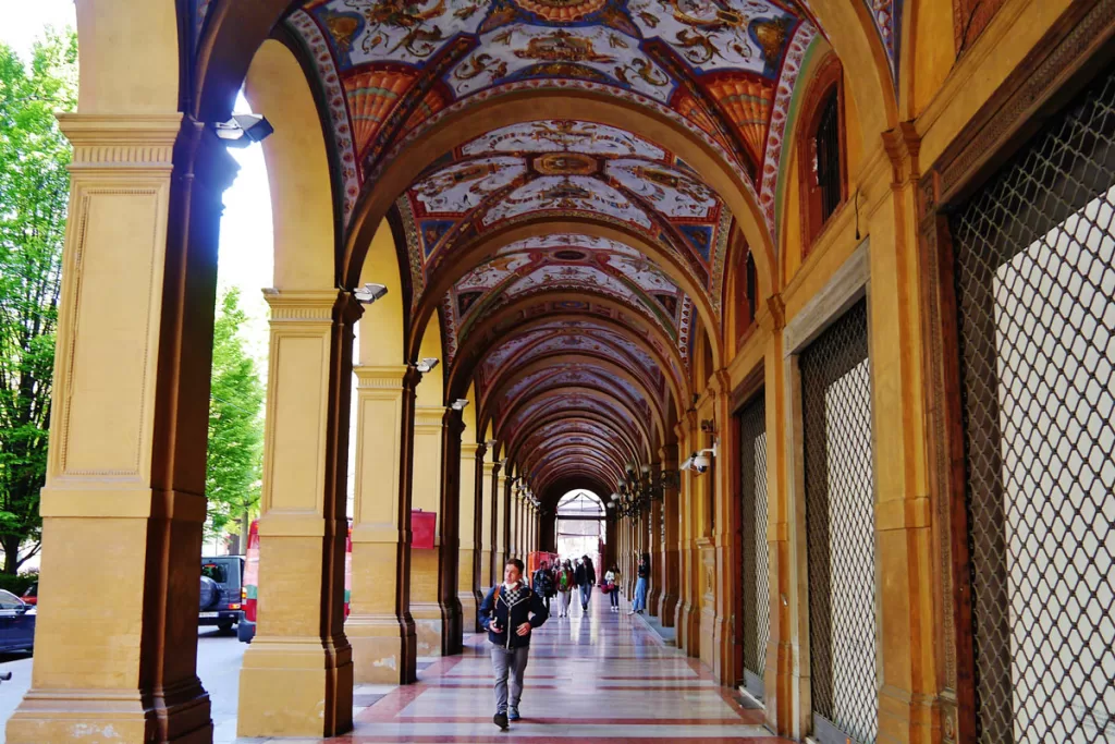 A solitary figure walks beneath the covered porticos near Piazza Cavour in Bologna, Italy.