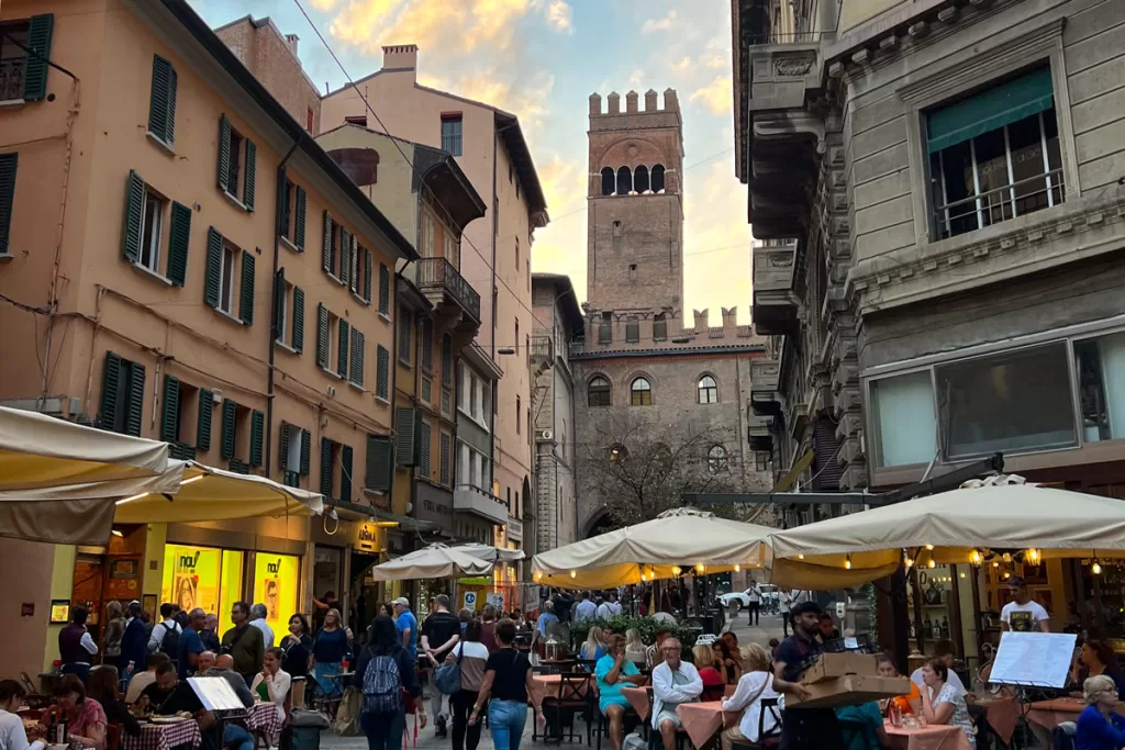 Patrons crowd the outdoor tables of Bologna's historic Quadrilatero district during evening aperitvo hour.