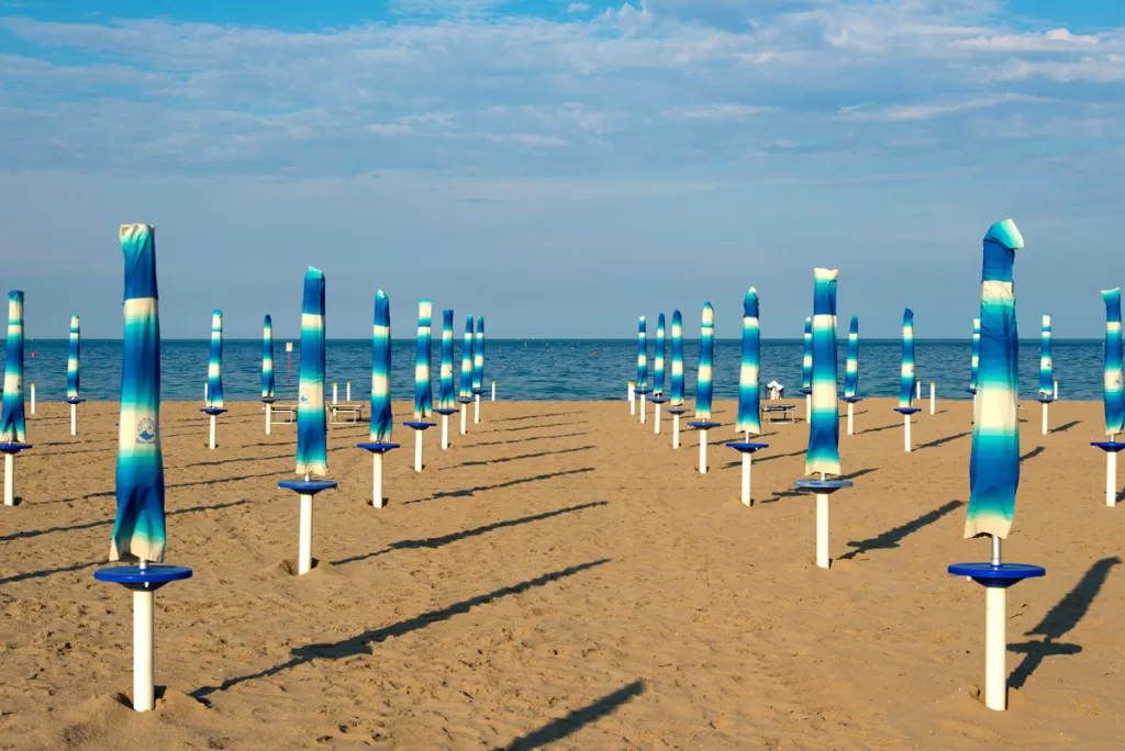 Blue and white beach umbrellas stretch in uniform lines along the sand to the water's edge in Rimini, Italy, on the Adriatic Sea.