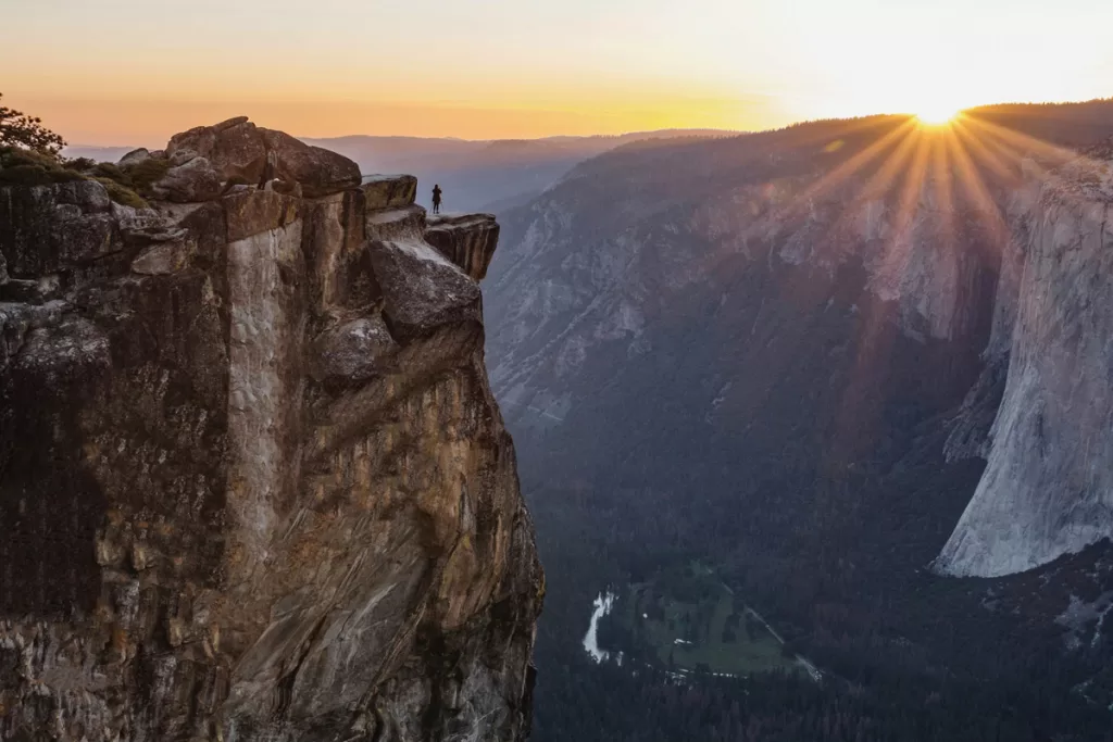 A solitary hiker stands on the cliff edge of Taft Point at sunset, overlooking Yosemite National Park.