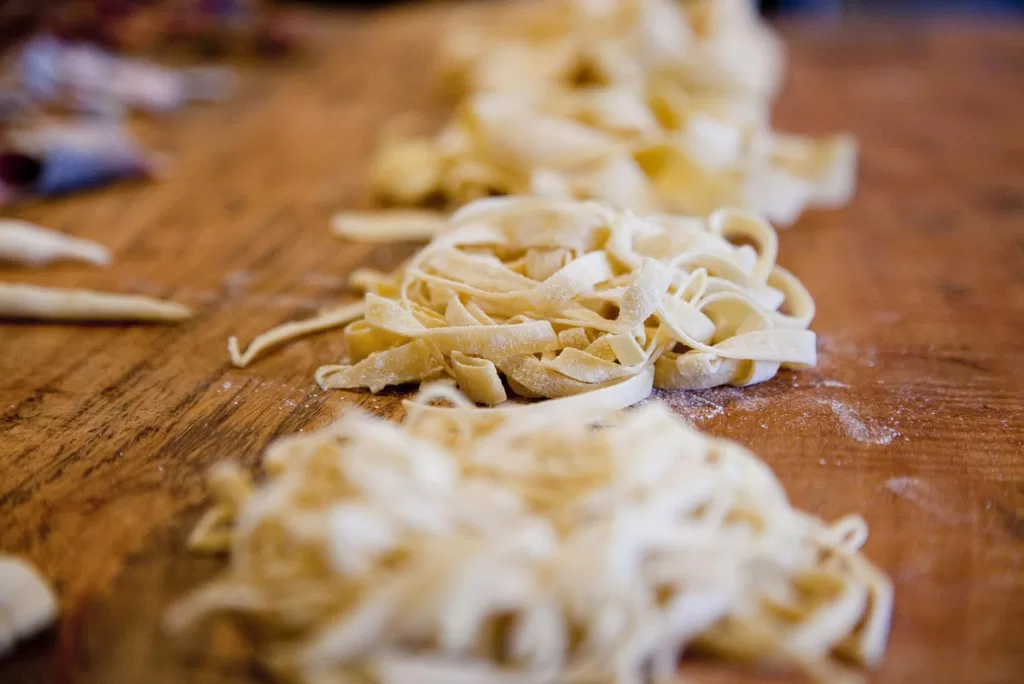 Mounds of dry tagliatelle noodles line a wooden table.