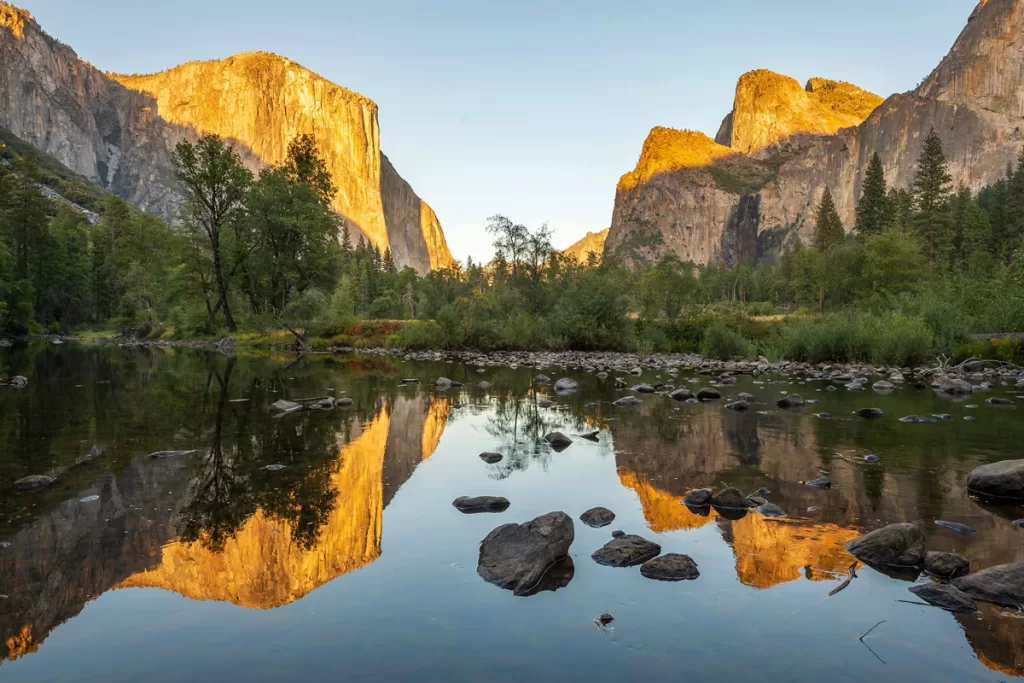 The granite peaks of El Capitan and Cathedral Rocks are clearly reflected in the placid waters of the Merced River, as seen from Valley View in Yosemite National Park.